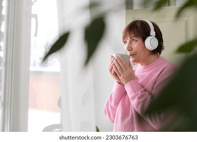 Senior lady in pink sweater finds joy in coffee and tunes - happiness at any age - Shutterstock ID 2303676763