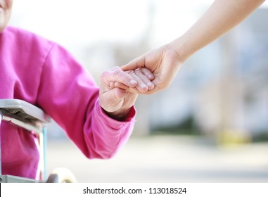 Senior Lady In Wheelchair Holding Hands With Caretaker