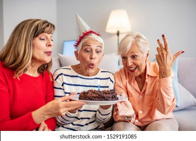 Senior Life Celebration. Birthday surprise party.Happy mature women celebrating birthday at home. Senior woman blow on birthday cake during a birthday party - Powered by Shutterstock