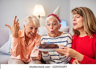 Senior Life Celebration. Birthday surprise party.Happy mature women celebrating birthday at home. Senior woman blow on birthday cake during a birthday party - Powered by Shutterstock