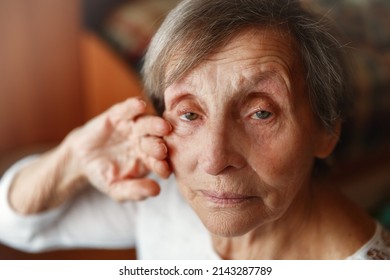 Senior lonely woman sitting at home and looking at camera. Old woman is crying and wipping away tears
