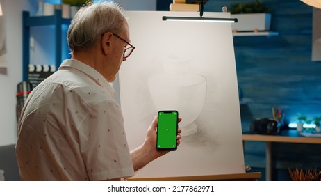 Senior Male Artist Holding Smartphone With Greenscreen To Draw Vase Artwork On Canvas At Home. Using Blank Template With Mockup Copyspace And Isolated Chroma Key Background On Mobile Phone.