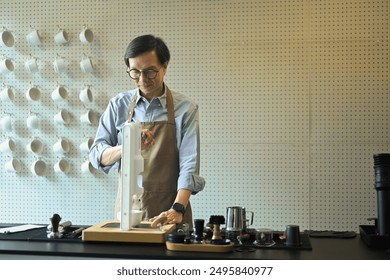 Senior male barista or coffee enthusiast wearing a brown apron using manual espresso machine in minimal coffee shop. - Powered by Shutterstock