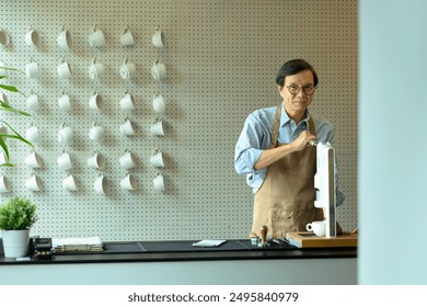 Senior male barista or coffee enthusiast wearing a brown apron using manual espresso machine in minimal coffee shop. - Powered by Shutterstock