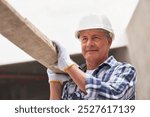 Senior male carpenter with planks on shoulder