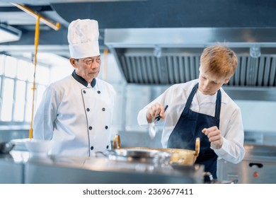 Senior male chef teaches young teenage boys cooking in school kitchen. Education Concept - Powered by Shutterstock