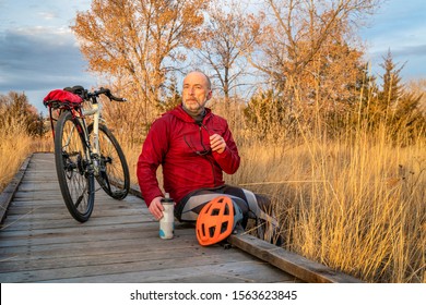 Senior Male Cyclist With A Touring Bike Is Taking A Rest At Wooden Boardwalk Across Swamp, Fall Sunset Scenery In Northern Colorado