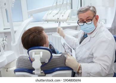 Senior Male Dentist Wearing Medical Face Mask, Looking To The Camera During Dental Appointment With Patient