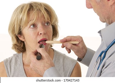 Senior Male Doctor Uses An Otoscope And Tongue Depressor To Look In A Senior Female Patient's Mouth. 