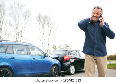 Senior Male Driver With Whiplash Injury Standing By Damaged Car After Traffic Accident Reporting Incident To Insurance Company Using Mobile Phone