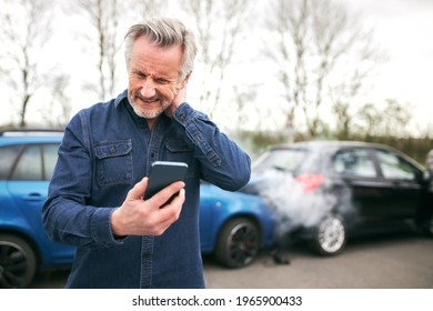 Senior Male Driver With Whiplash Injury Standing By Damaged Car After Traffic Accident Reporting Incident To Insurance Company Using Mobile Phone