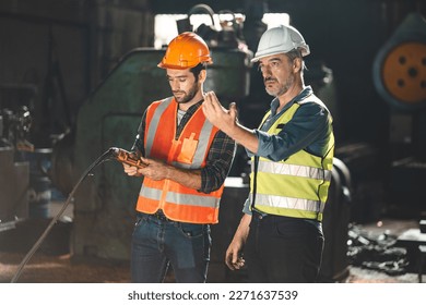 Senior male engineer training and explaining work to new employee wearing vest and safety jacket with hardhat helmet while pointing towards machine in factory and giving instructions - Powered by Shutterstock