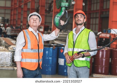 senior male factory owner and male worker wearing safety helmets look at a crane lifting loads in a warehouse inspecting its operation. - Powered by Shutterstock