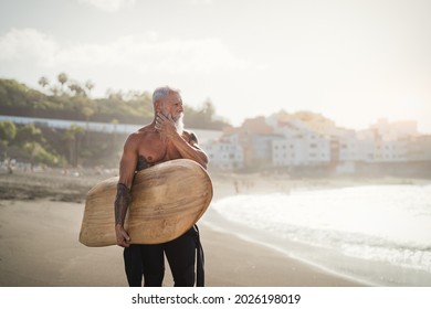 Senior male having fun surfing during sunset time - Fit retired man training with surfboard on the beach - Elderly healthy people lifestyle and extreme sport concept - Powered by Shutterstock