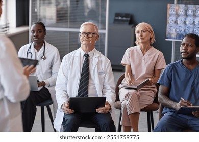 Senior male head physician listening to colleagues presentation with diverse team of doctors while participating in seminar at conference room - Powered by Shutterstock