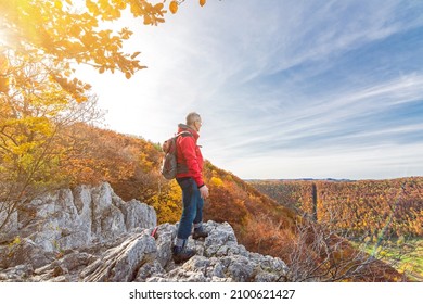 Senior male hiker standing on a cliff ledge and looking at a colourful hilly autumn landscape in the Swabian Jura - Powered by Shutterstock