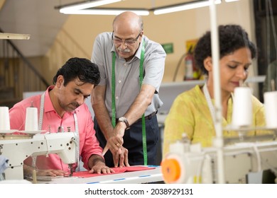 Senior Male Instructors Explaining Textile Worker Sewing Garment On Production Line