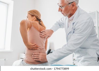 Senior male orthopedist examining patient's back in clinic - Powered by Shutterstock