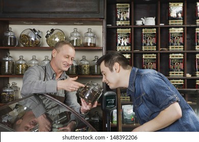 Senior Male Owner Showing Tea Jar To Customer Shop