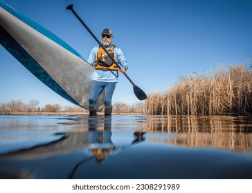 senior male paddler is launching a stand up paddleboard on a calm lake in early spring, frog perspective from an action camera at water level - Powered by Shutterstock