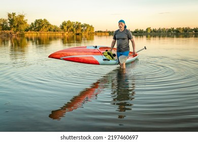 Senior Male Paddler With A Long And Narrow Racing Stand Up Paddleboard On A Calm Lake At Sunset.