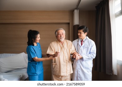 Senior Male Patient Sitting On Wheelchair In Hospital Smiling And Talking And Showing Something Outside The Window To Handsome Doctor In Labcoat In Room