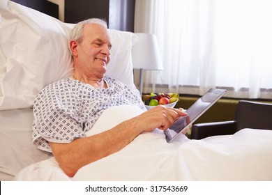 Senior Male Patient Using Digital Tablet In Hospital Bed