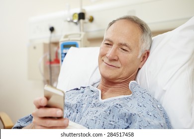 Senior Male Patient Using Mobile Phone In Hospital Bed