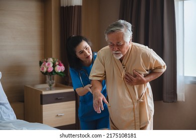 Senior Male Patient Wearing Gown Admitted In Hospital Holding Chest Due To Pain Suffering From Heart Attack While Holding And Taking Support Of Window In Ward And Private Room