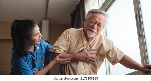 Senior Male Patient Wearing Gown Admitted In Hospital Holding Chest Due To Pain Suffering From Heart Attack While Holding And Taking Support Of Window In Ward And Private Room