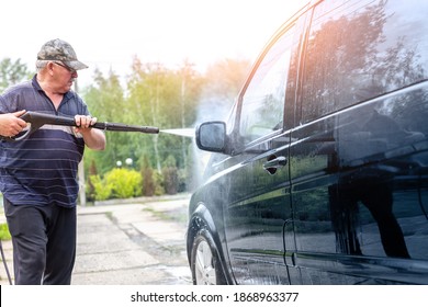 Senior Male Person Wash Car Van With High Pressure Water Equipment Pump At Home Backyard Outdoors On Bright Shiny Summer Day. Vehicle Covered With Foam Chemical Detergents During Carwash Self Service