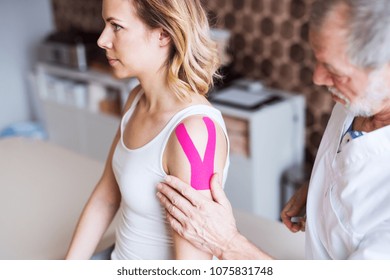 Senior male physiotherapist applying tape on a female patient. - Powered by Shutterstock