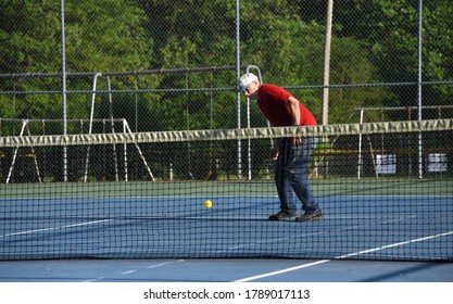 Senior Male Pulls Racket Back For Swing At Yellow Pickle Ball.  He Is Playing On A Tennis Court Outdoors.