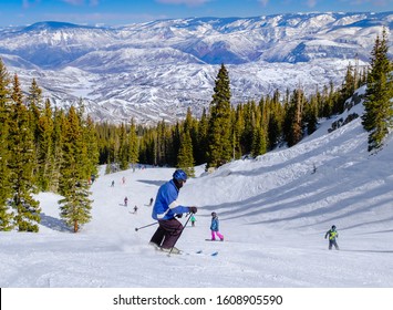 
Senior male skier skiing in Colorado ski resort near Aspen, Colorado, on nice winter day; more skiers and snowboarders skiing around; woods and mountains in background