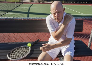 Senior male tennis player with shoulder pain sitting on bench at court - Powered by Shutterstock