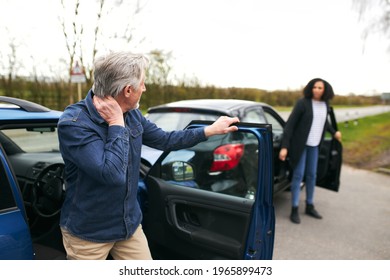 Senior male and younger female drivers get out of cars and inspect damage after road traffic accident