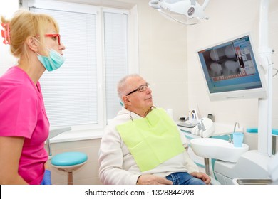 Senior Man 75 Years Old On A Review Of A Dentist, Sitting In A Chair. Dentist Female Explaining X-Ray To Older Man. Dental Care For Older People. Dentistry, Medicine And Health Care Concept