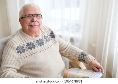 Senior Man 75-75 Years Old Sitting At Home And Reading Book In Armchair. Old Age, Lifestyle And People Concept