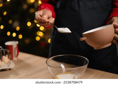 Senior man adding sugar into bowl while preparing holiday cookies in festive kitchen setting. Warm Christmas lights illuminate cozy space, emphasizing joyful holiday baking tradition. - Powered by Shutterstock