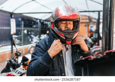 A senior man adjusting his red and black motorcycle helmet while preparing for a ride outdoors - Powered by Shutterstock