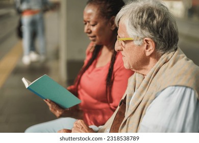 Senior man and african mature woman sitting together at tram station - Elderly nursing care concept - Powered by Shutterstock