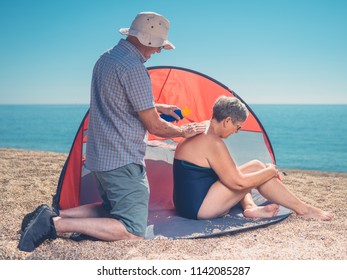 A Senior Man Is Applying Sun Cream To His Wife's Back