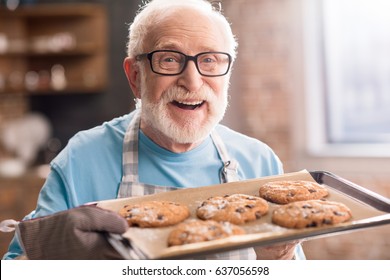 Senior man in apron holding tray of delicious cookies, cooking in kitchen concept - Powered by Shutterstock