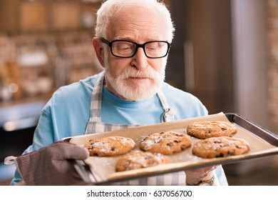 Senior man in apron holding tray of delicious cookies, cooking in kitchen concept - Powered by Shutterstock