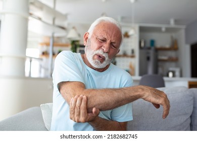 Senior Man With Arm Pain.Old Male Massaging Painful Hand Indoors. Old Man Hand Holding His Elbow Suffering From Elbow Pain. Senior Man Suffering From Pain In Hand At Home. Old Age, Health