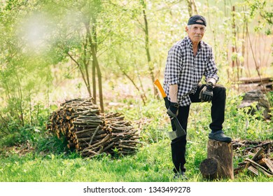 Senior Man With Axe Chopping Wood. Elderly Arborist Man Working In Garden. Active Retirement Lifestyle Concept.