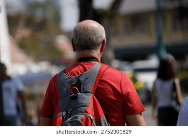 Senior man with backpack walking exploring, walking motion, step movement, daily commute, routine city travel, bald man, rear view, at Tha Chang.