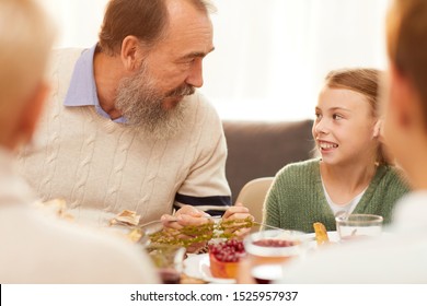 Senior Man With Beard Talking To His Granddaughter While They Eating At Dining Table During Family Dinner