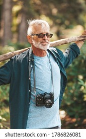 Senior Man With Beard Walks Through Woods, Healthy Active Lifestyle. Vertical Portrait Of Senior Citizen With Camera In Park.