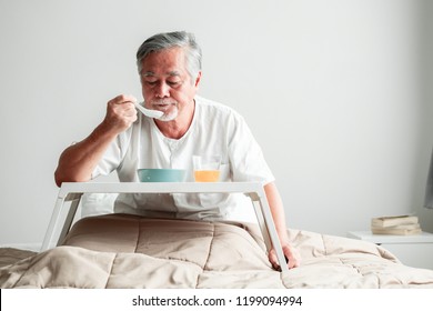 Senior Man In Bed Enjoying Breakfast. Old Asian Male With White Beard Eating Congee And Orange Juice. Senior Home Service Concept.